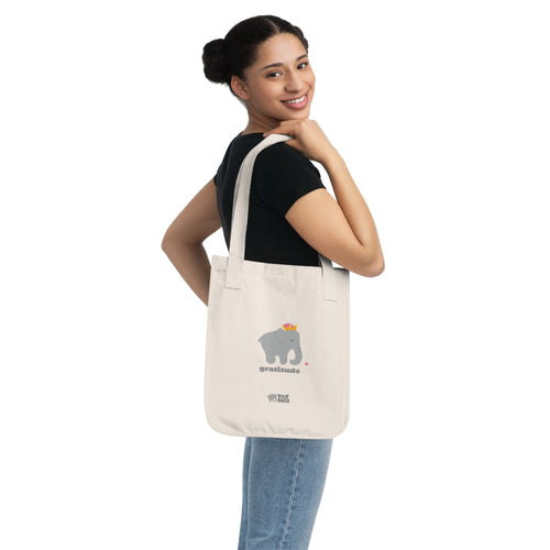 Woman carrying a natural beige canvas tote bag with printed design; a gray elephant and 'gratitude' text with colorful hearts on a white background.