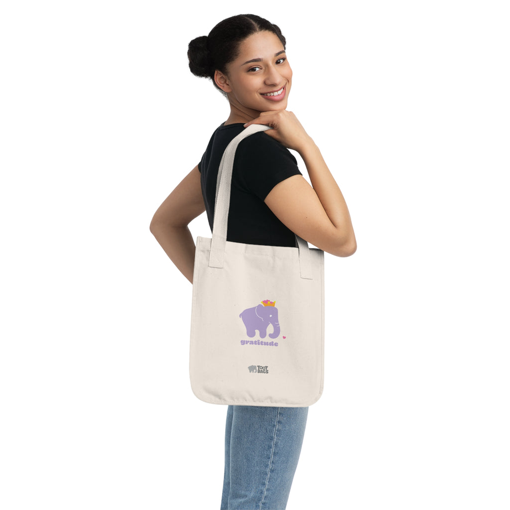 Woman carrying a beige natural canvas tote bag with printed design; a purple elephant and 'gratitude' text with colorful hearts on a white background.
