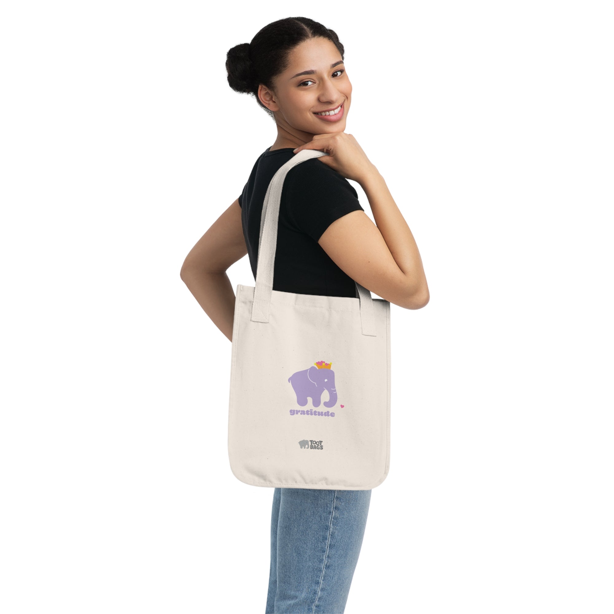 Woman carrying a beige natural canvas tote bag with printed design; a purple elephant and 'gratitude' text with colorful hearts on a white background.