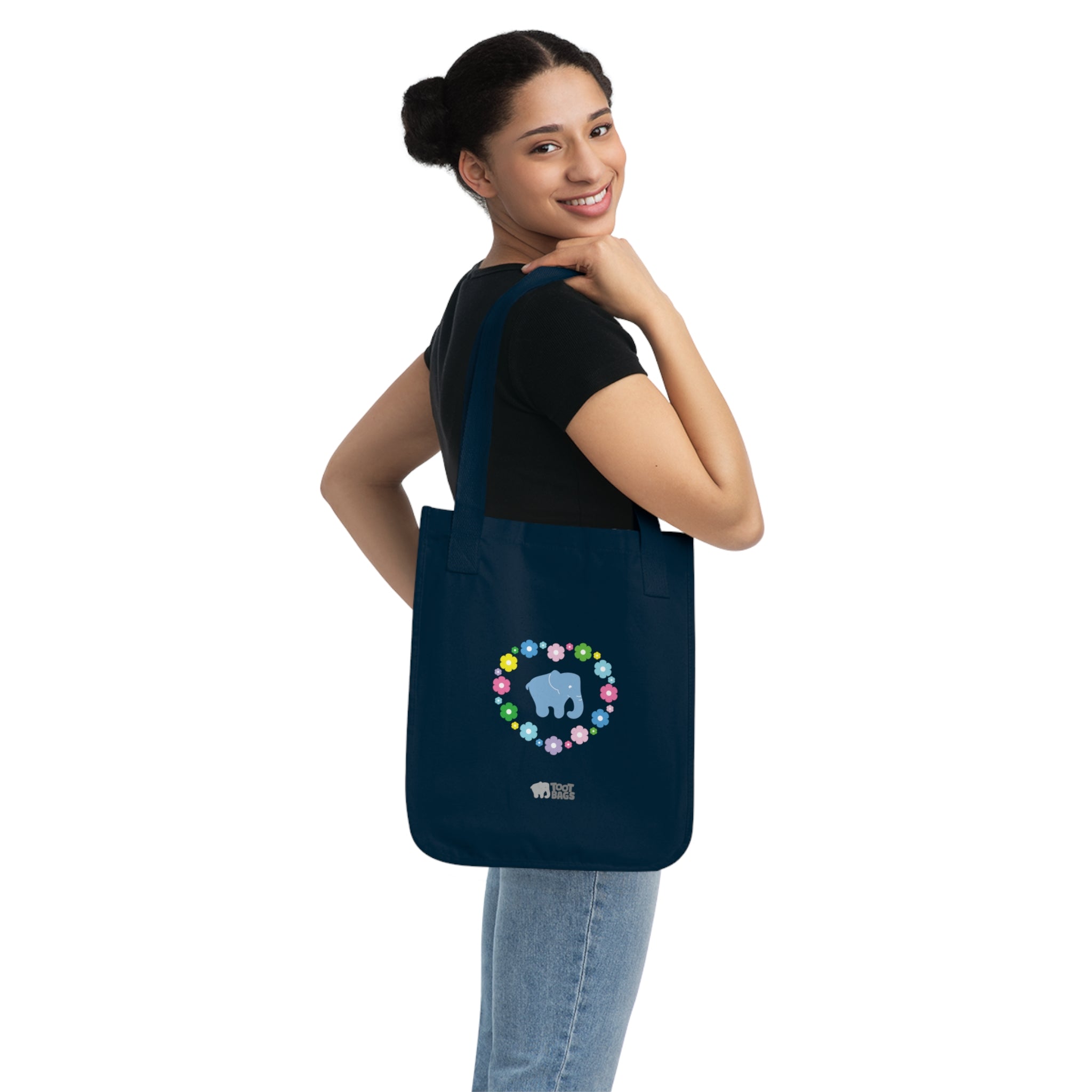 Woman carrying a navy blue canvas tote bag featuring a colorful printed design; a blue elephant with floral heart shaped design on a white background.  