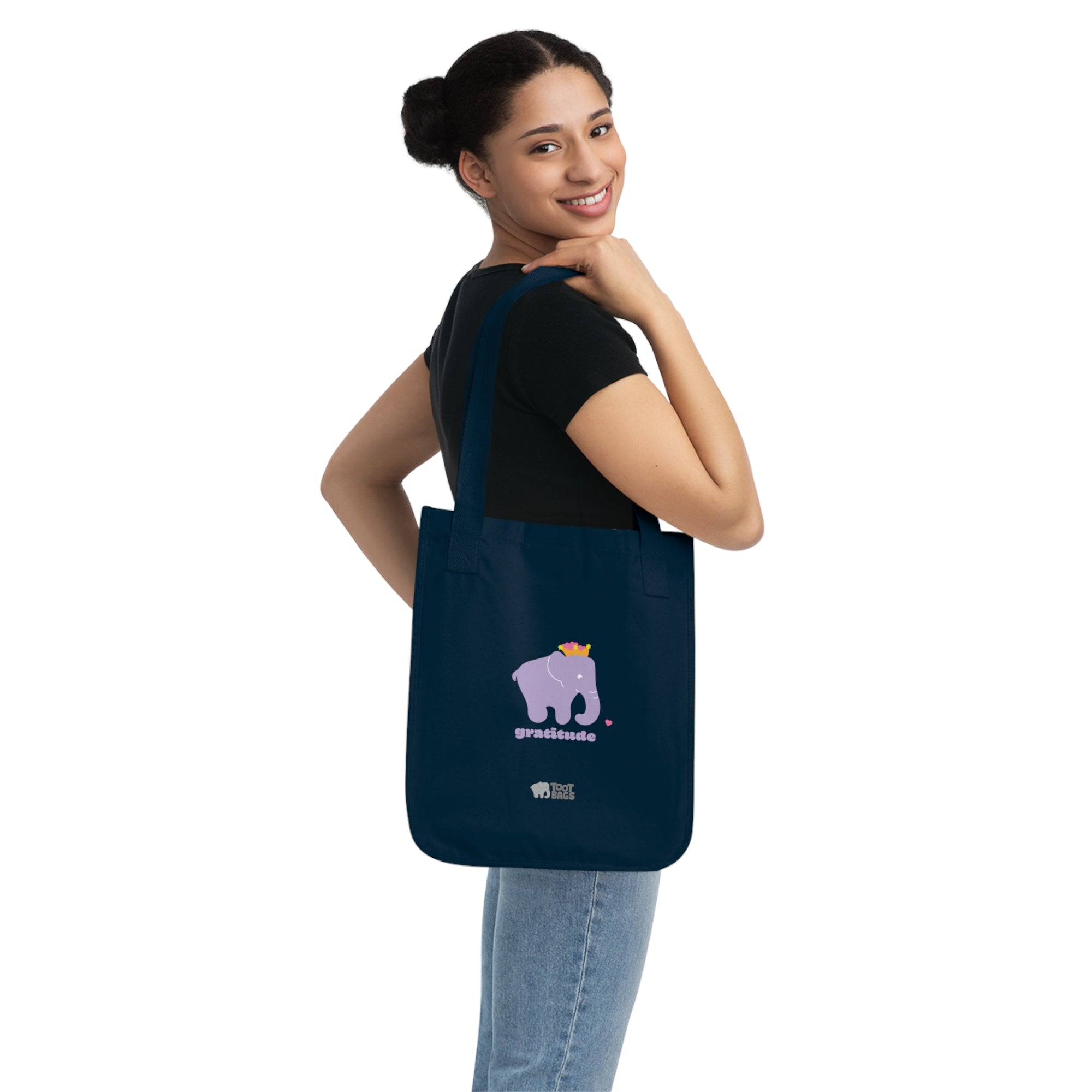 Woman carrying a navy blue canvas tote bag with printed design; a purple elephant and gratitude text with colorful hearts on a white background.