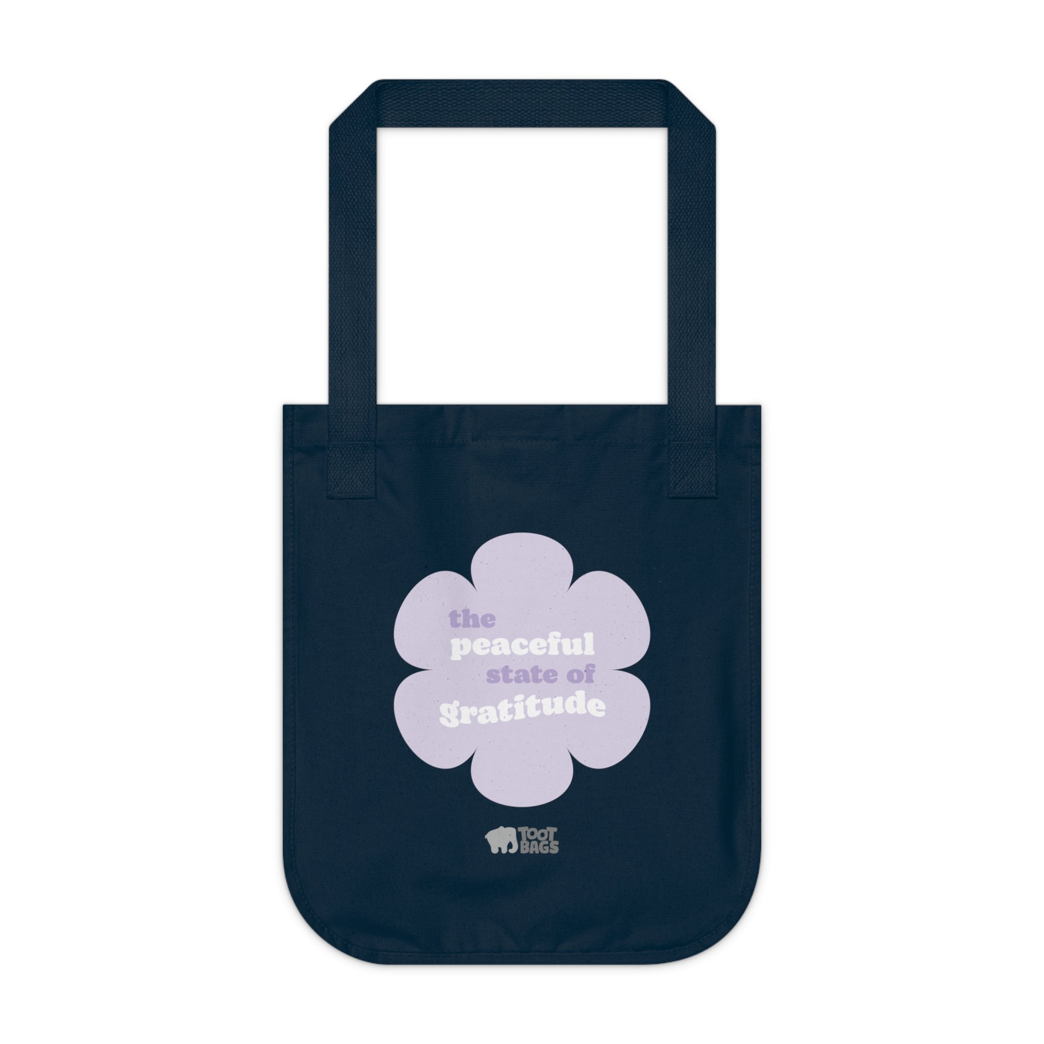 Navy blue canvas tote bag with a printed design featuring a purple flower and ‘the peaceful state of gratitude’ text design in purple and white placed on a white background.