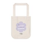 Natural beige canvas tote bag with a printed design featuring a purple flower and ‘the peaceful state of gratitude’ text design in purple and white placed on a white background.
