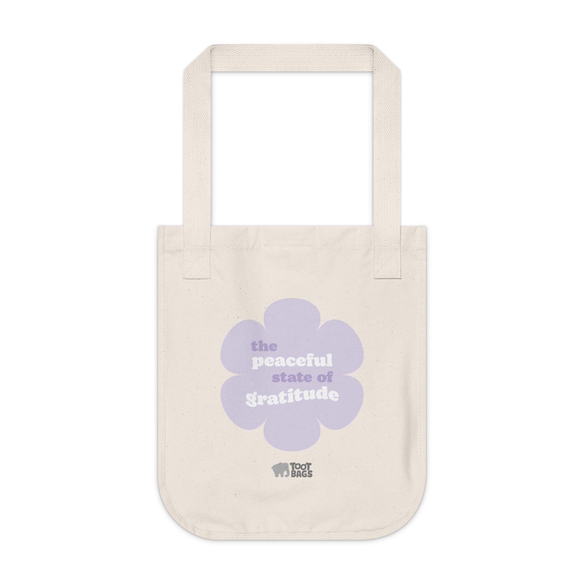 Natural beige canvas tote bag with a printed design featuring a purple flower and ‘the peaceful state of gratitude’ text design in purple and white placed on a white background.