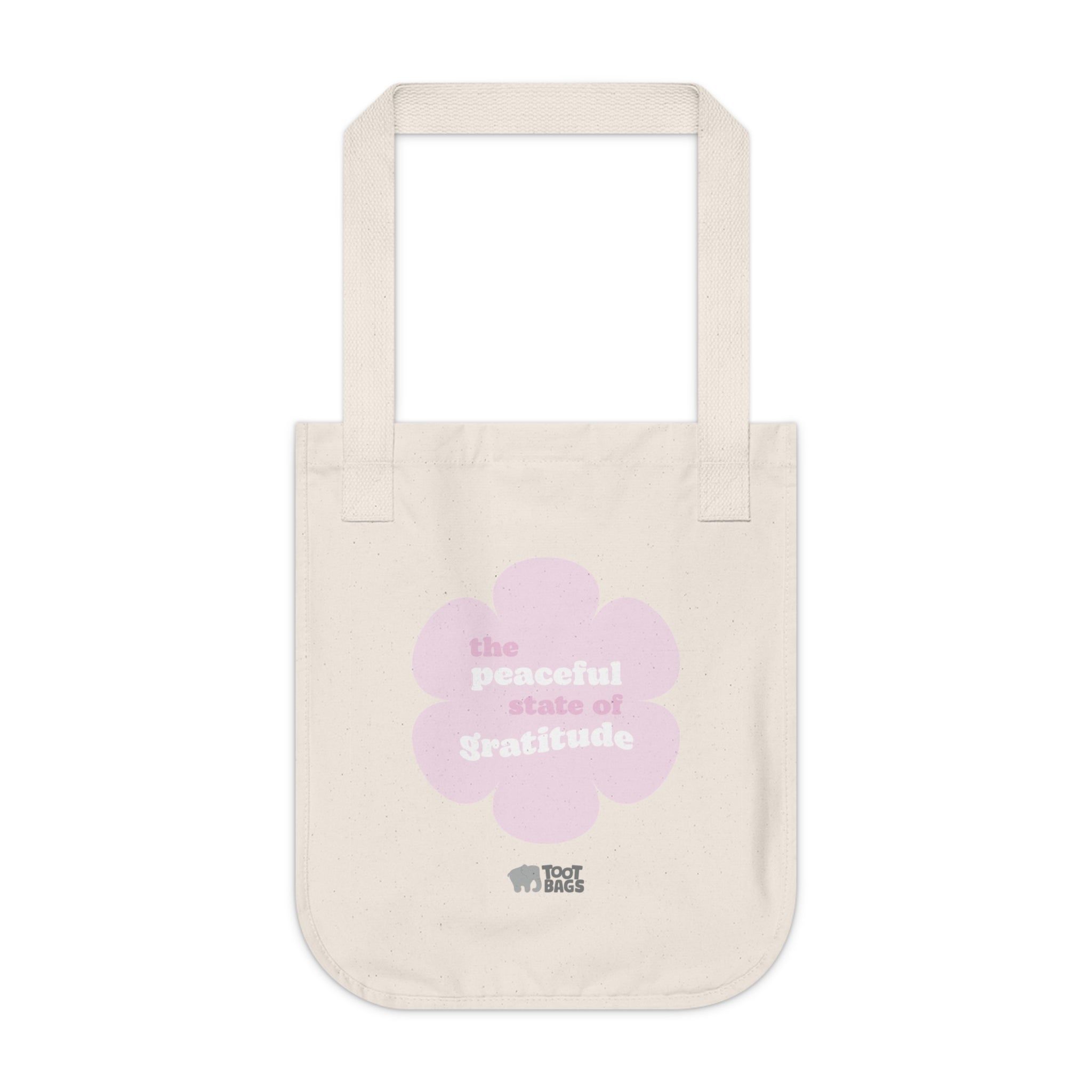 Natural beige canvas tote bag with a printed design featuring a pink flower and ‘the peaceful state of gratitude’ text design placed on a white background.