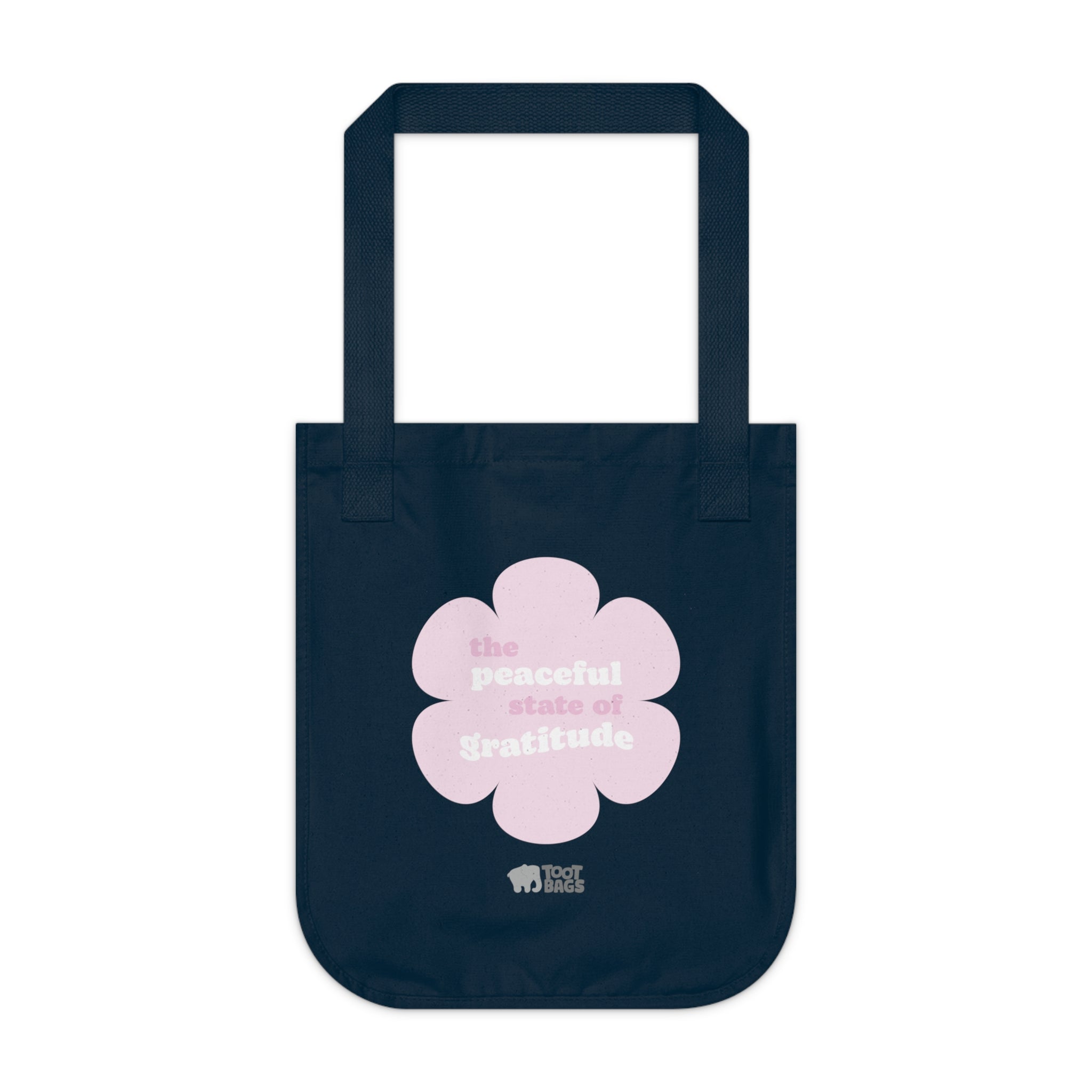 Navy blue canvas tote bag with a printed design featuring a pink flower and ‘the peaceful state of gratitude’ text design placed on a white background.