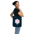 Woman holding a navy blue canvas tote bag with a printed design featuring a pink flower and ‘the peaceful state of gratitude’ text design on a white background.
