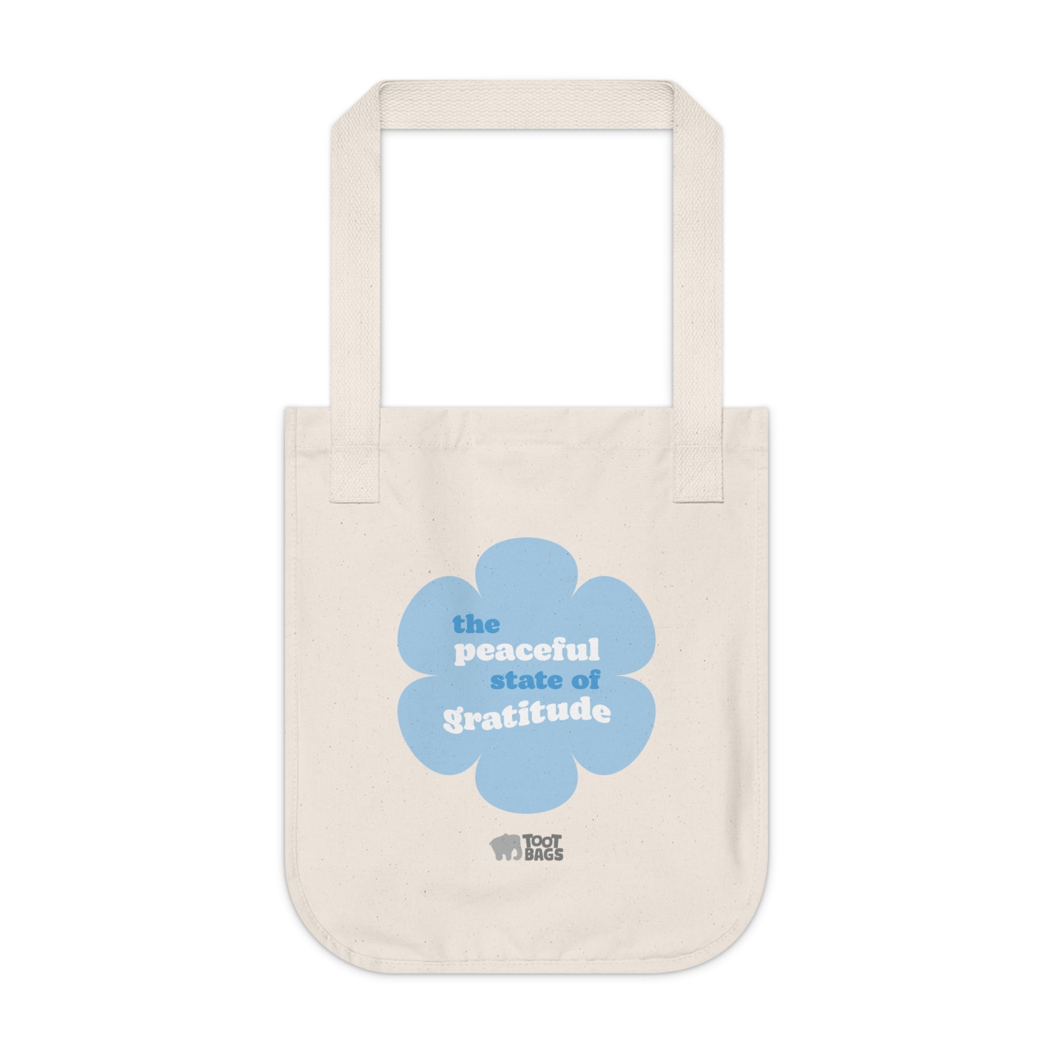 Natural beige canvas tote bag with a printed design featuring a blue flower and ‘the peaceful state of gratitude’ text design on a white background.