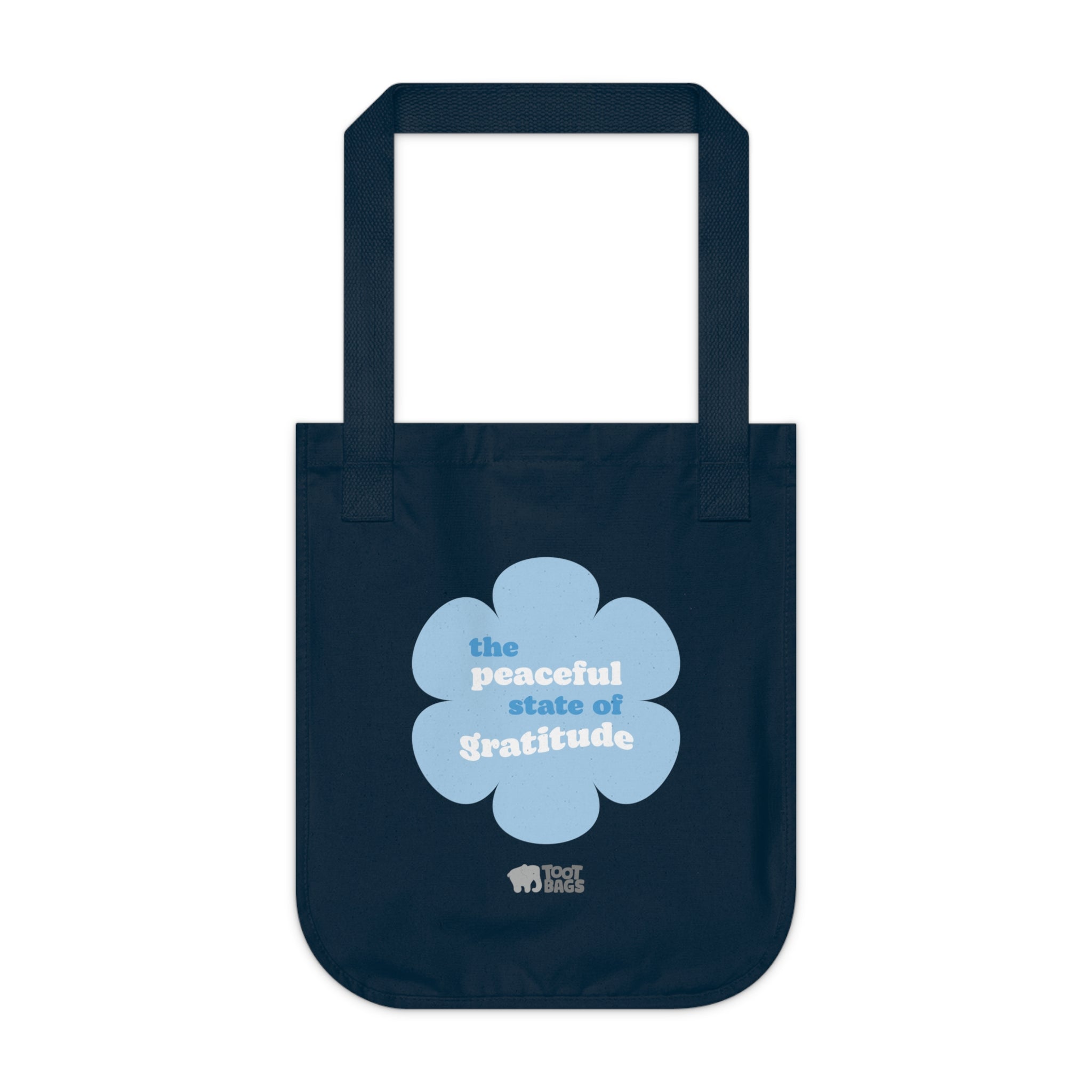 Navy blue canvas tote bag with a printed design featuring a blue flower and ‘the peaceful state of gratitude’ text design on a white background.