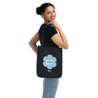 Woman holding a black canvas tote bag with a printed design featuring a blue flower and ‘the peaceful state of gratitude’ text design on a white background.